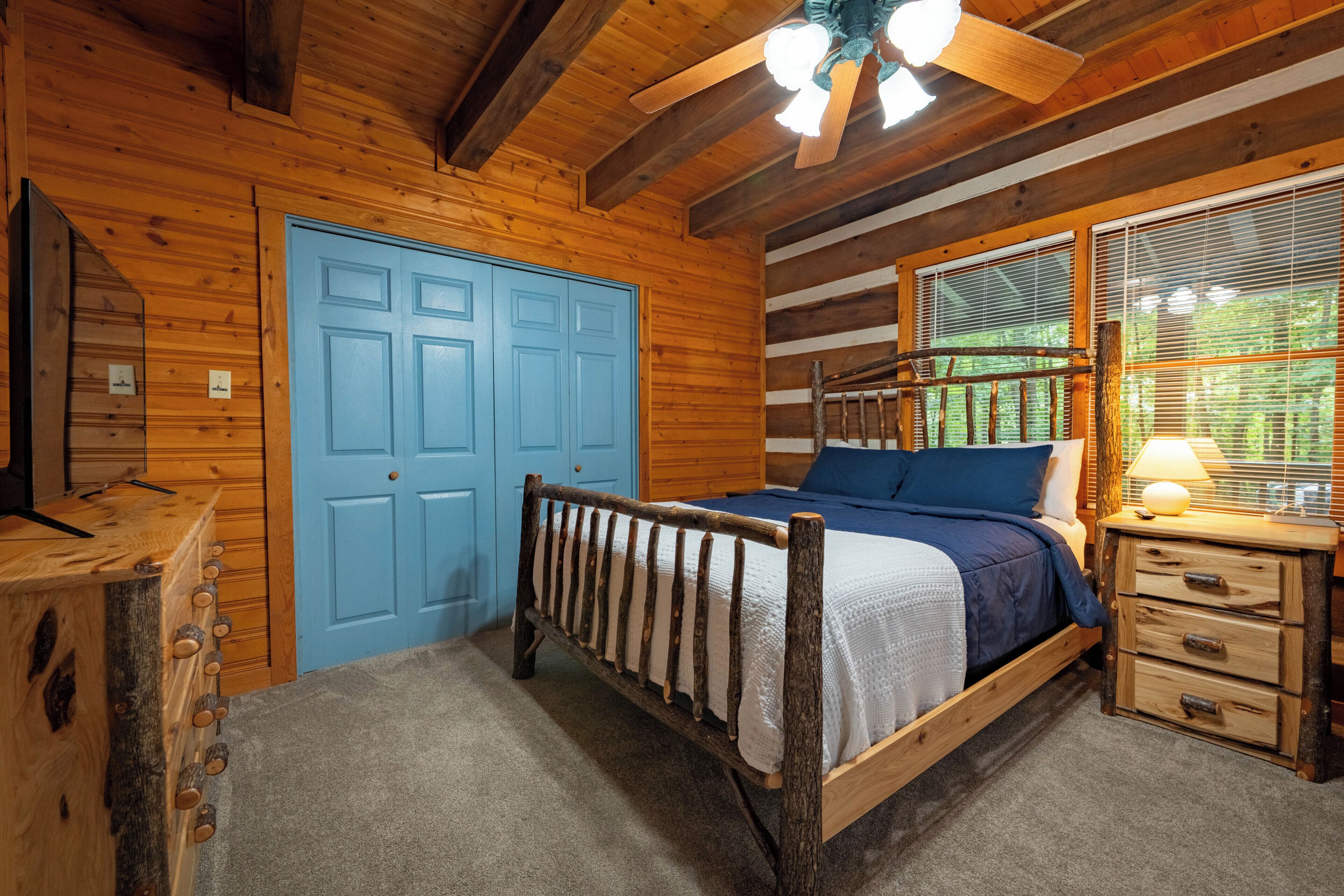 Une chambre dans une cabane en bois, avec un lit, une commode et une porte bleue.