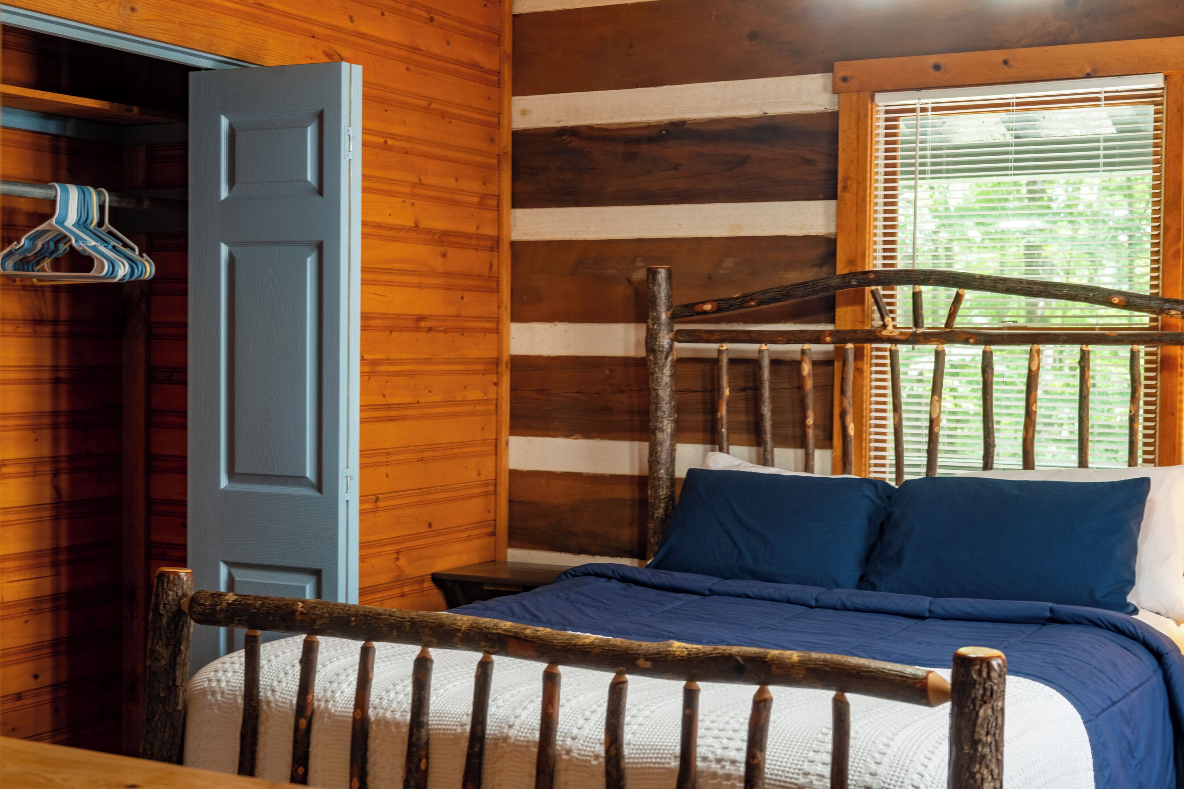 Une chambre dans un chalet en bois, avec un lit, une armoire et une fenêtre équipée de stores.