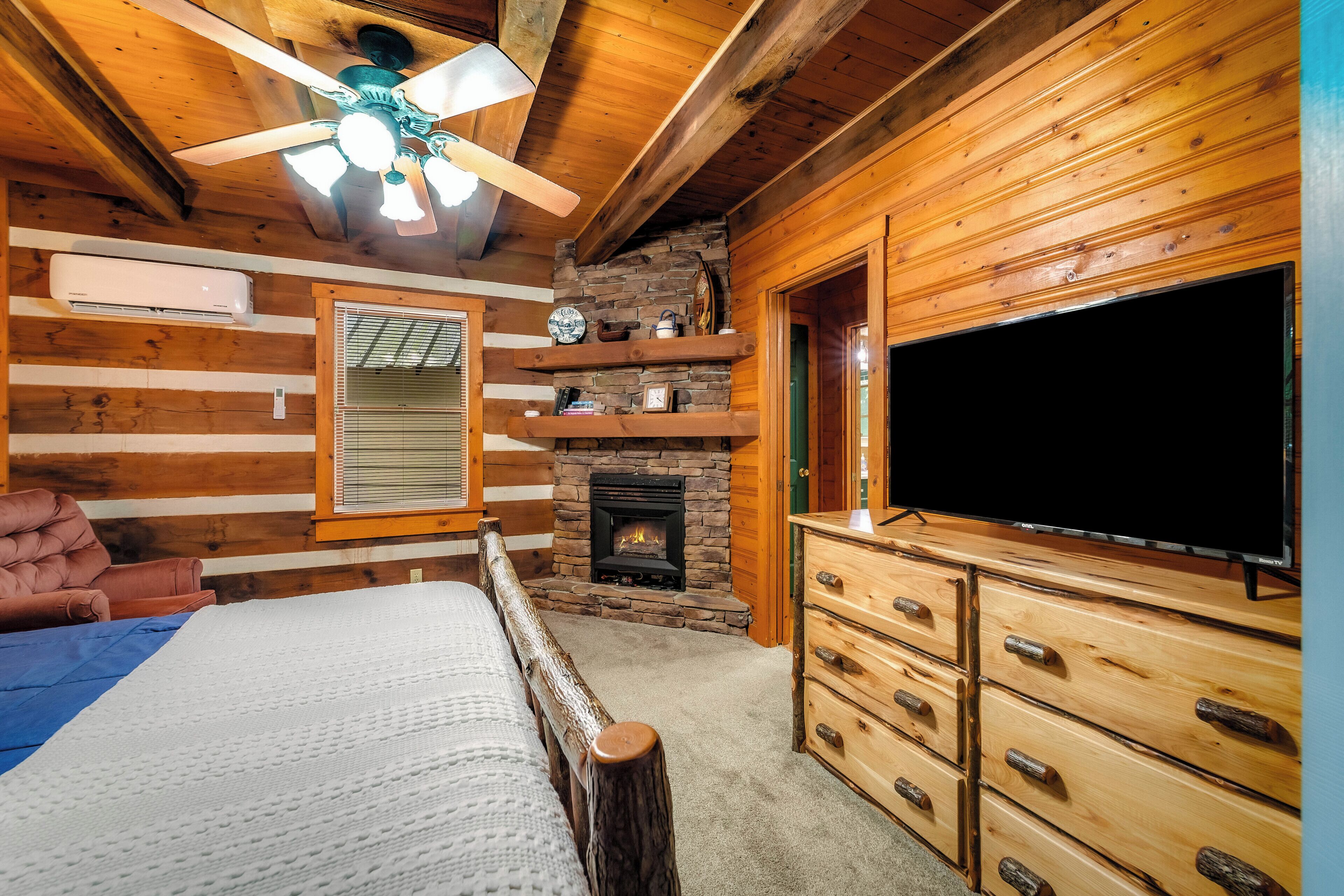 Ein rustikales Blockhaus-Interieur mit einem Bett, einem Kamin, einem Fernseher und einem Deckenventilator.