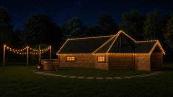 A wooden cabin with string lights, a fire pit, and a clear night sky.