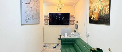 A modern living room with a green sofa, a flat-screen TV, and a chandelier.
