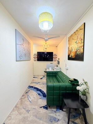 A modern living room with a green sofa, a flat-screen TV, and a chandelier. - TIDY Premium Stay Dubai (Dubai)
