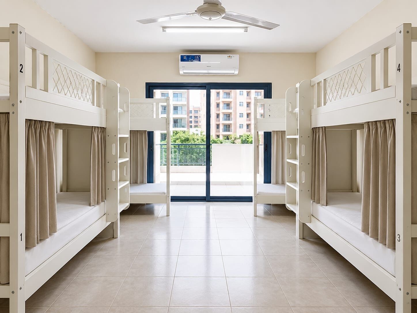 A hotel room with bunk beds, a ceiling fan, an air conditioning unit, and a view of a residential area.
