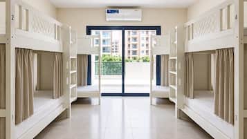 A hotel room with bunk beds, a ceiling fan, an air conditioning unit, and a view of a residential area.