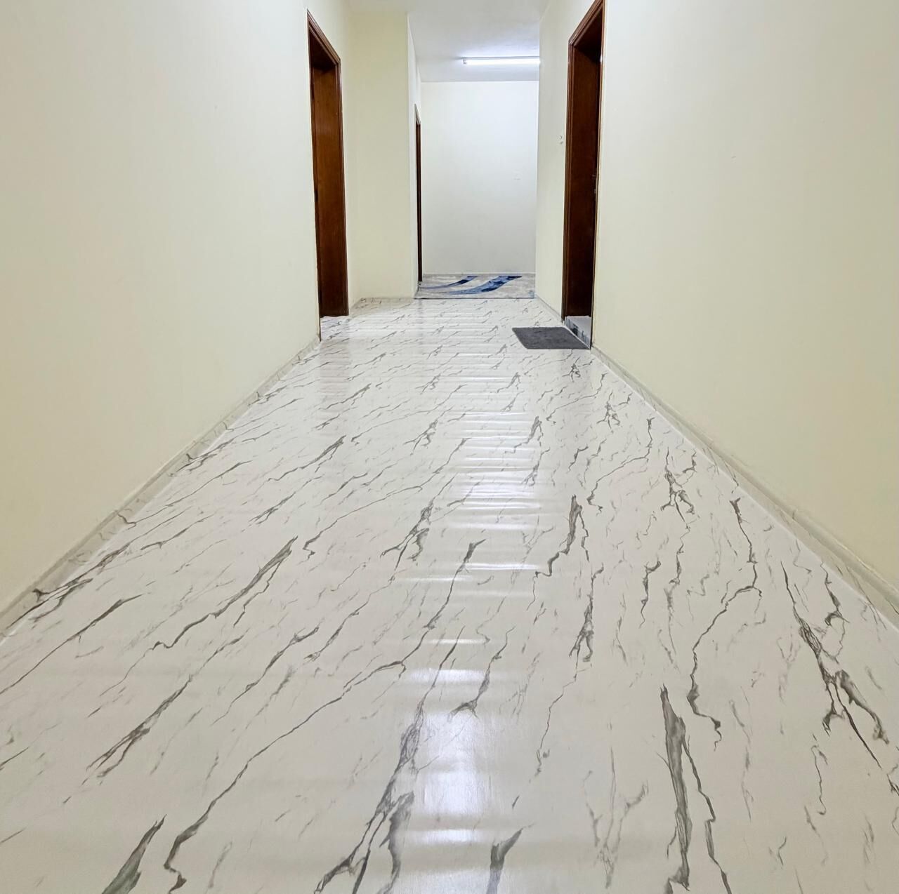 A hallway with a marble floor, wooden doors, and a light fixture on the ceiling.