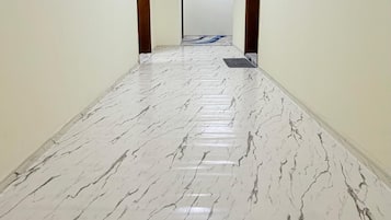 A hallway with a marble floor, wooden doors, and a light fixture on the ceiling.
