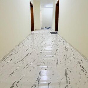 A hallway with a marble floor, wooden doors, and a light fixture on the ceiling.