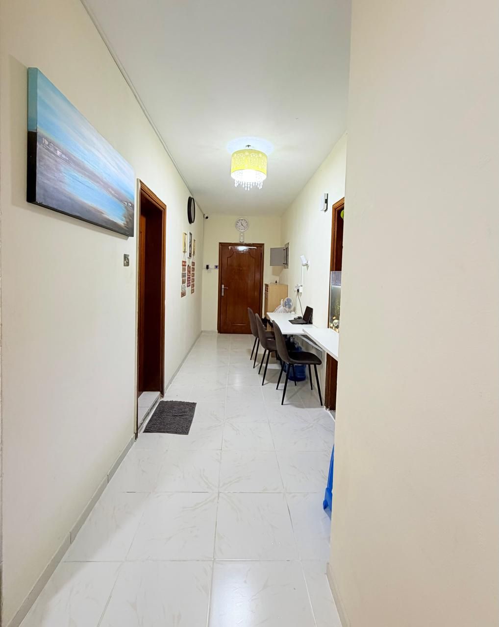 A hallway with a dining area, a clock on the wall, and a ceiling light fixture.