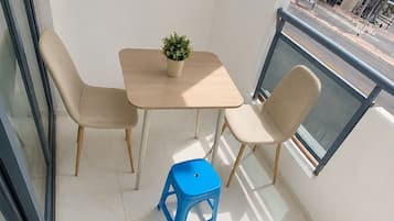Een balkon met een tafel, stoelen, een plant in pot en een blauwe kruk.