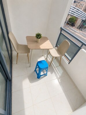A balcony with a table and chairs, a potted plant, and a blue stool.
