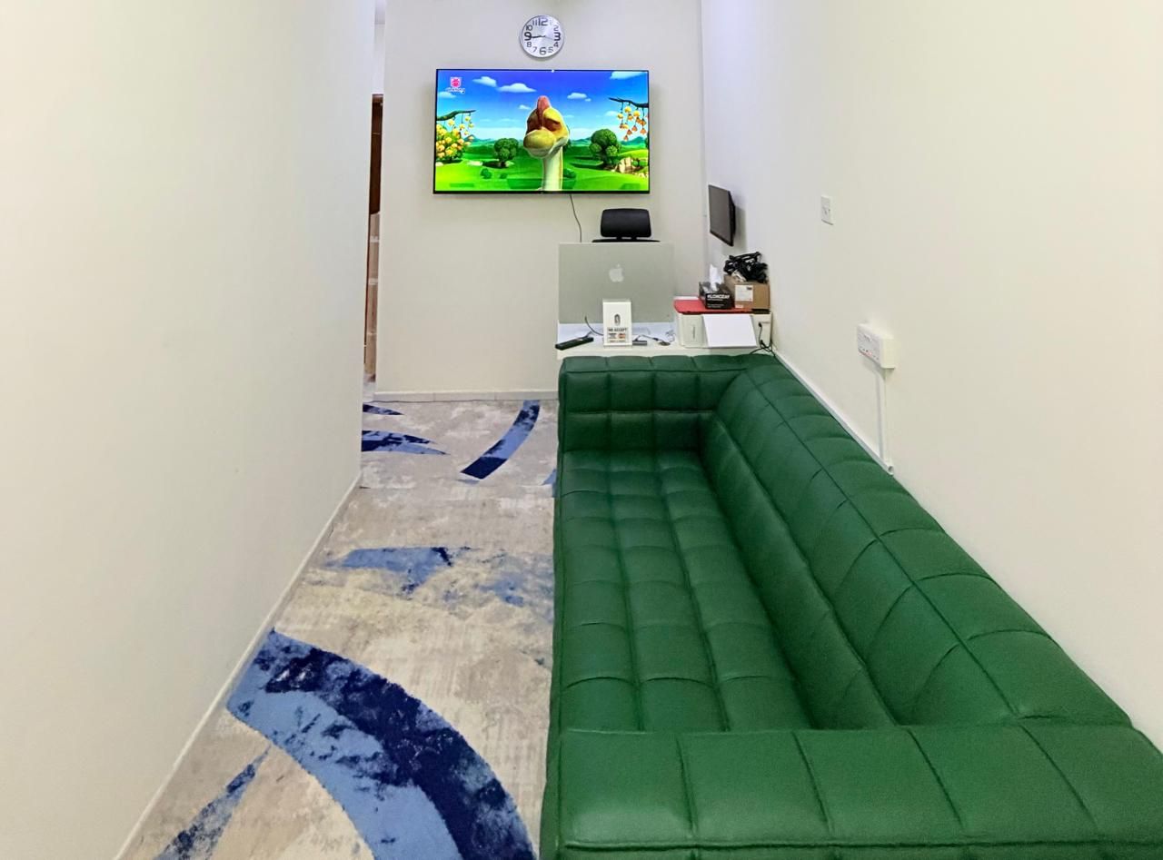 Een kamer met een groene bank, een flatscreen televisie aan de muur en een bureau met een computer.