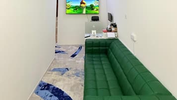 Een kamer met een groene bank, een flatscreen televisie aan de muur en een bureau met een computer.