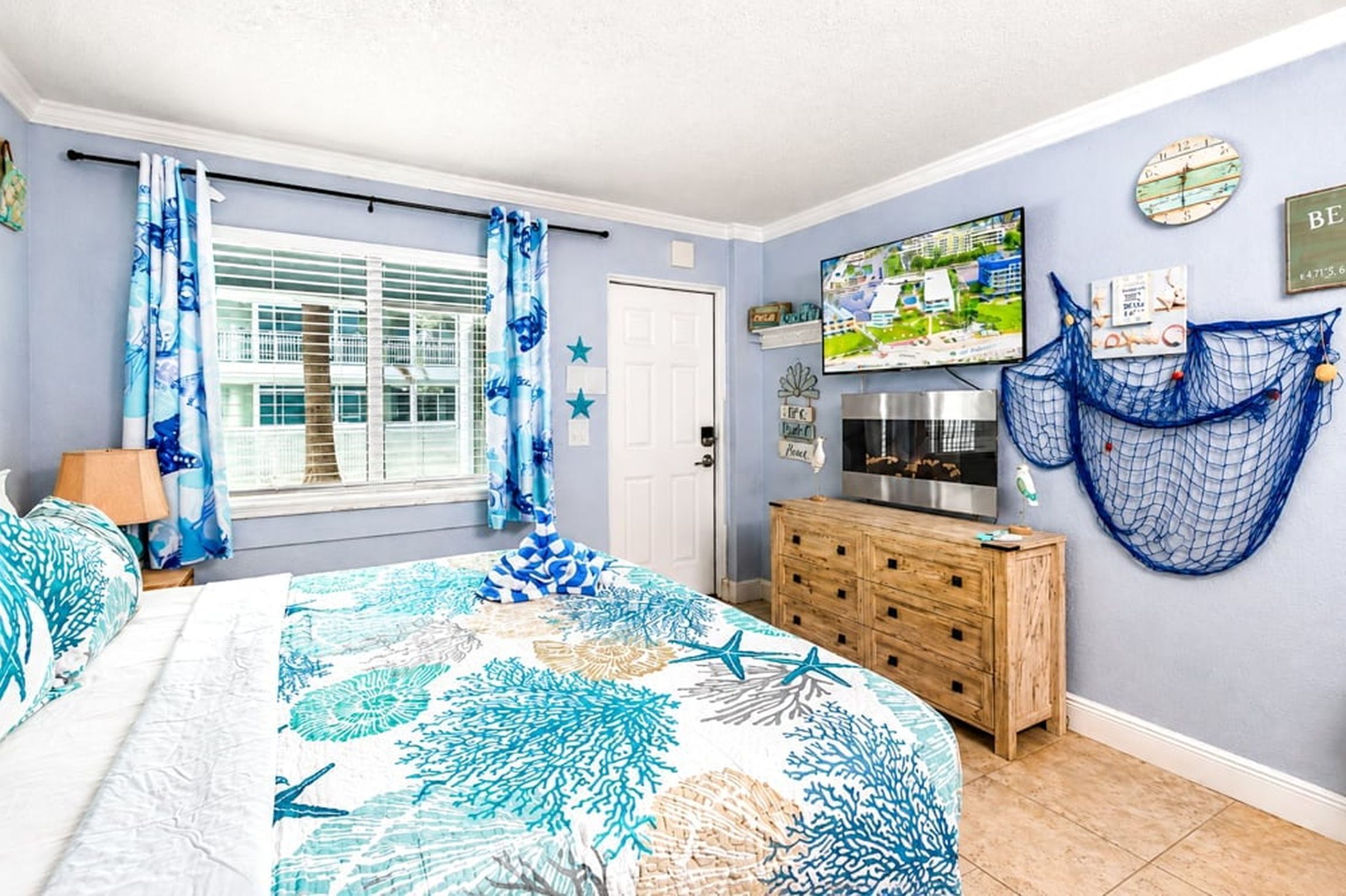 Een slaapkamer met een bed, een houten dressoir, een televisie en een raam met gordijnen.