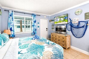 Une chambre à coucher avec un lit, une commode en bois, un téléviseur et une fenêtre avec des rideaux.