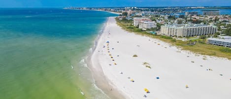 Uma praia com uma extensa faixa de areia, alguns guarda-sóis e edifícios ao fundo.