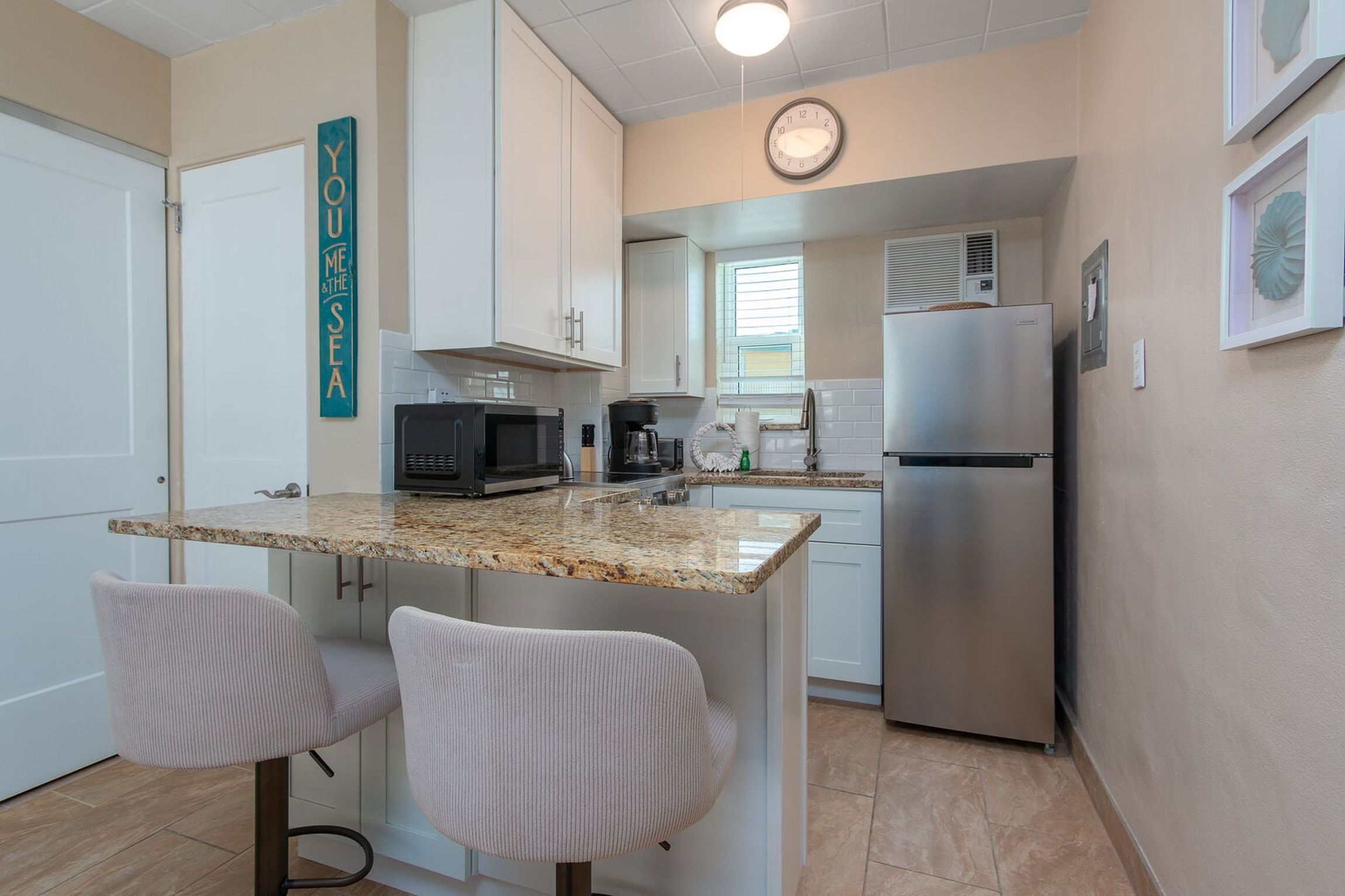 A compact kitchen with a microwave, coffee maker, and refrigerator. There are two chairs and a small island with a sink.