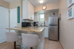 A compact kitchen with a microwave, coffee maker, and refrigerator. There are two chairs and a small island with a sink. - 🌴Pool/Shuffleboard/Grills🌞Beachfront Property🐠Tropic Terrace 18 (Treasure Island)