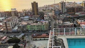 Un immeuble de grande hauteur doté d’une piscine, entouré d’autres bâtiments et bordé par un plan d’eau.