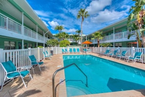 A hotel pool area with a clear blue pool, white railings, and multiple lounge chairs. - 🌴Easy Beach Access ☀️ Community Pool/Shuffleboard/Cornhole 🐠 Tropic Terrace #22 (Treasure Island)