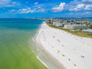 A beach with a long stretch of sand, a few umbrellas, and buildings in the background. - 🌴Easy Beach Access ☀️ Community Pool/Shuffleboard/Cornhole 🐠 Tropic Terrace #22 (Treasure Island)