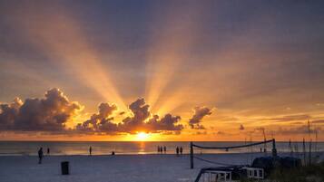 A beach with a volleyball net, people walking, and a sunset.