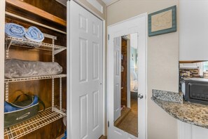 Un armario con estantes, una puerta que da a una habitación y una zona de cocina con microondas.