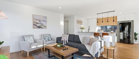 A modern living room with a sofa, chairs, a coffee table, and a kitchen area with a refrigerator and cabinets.