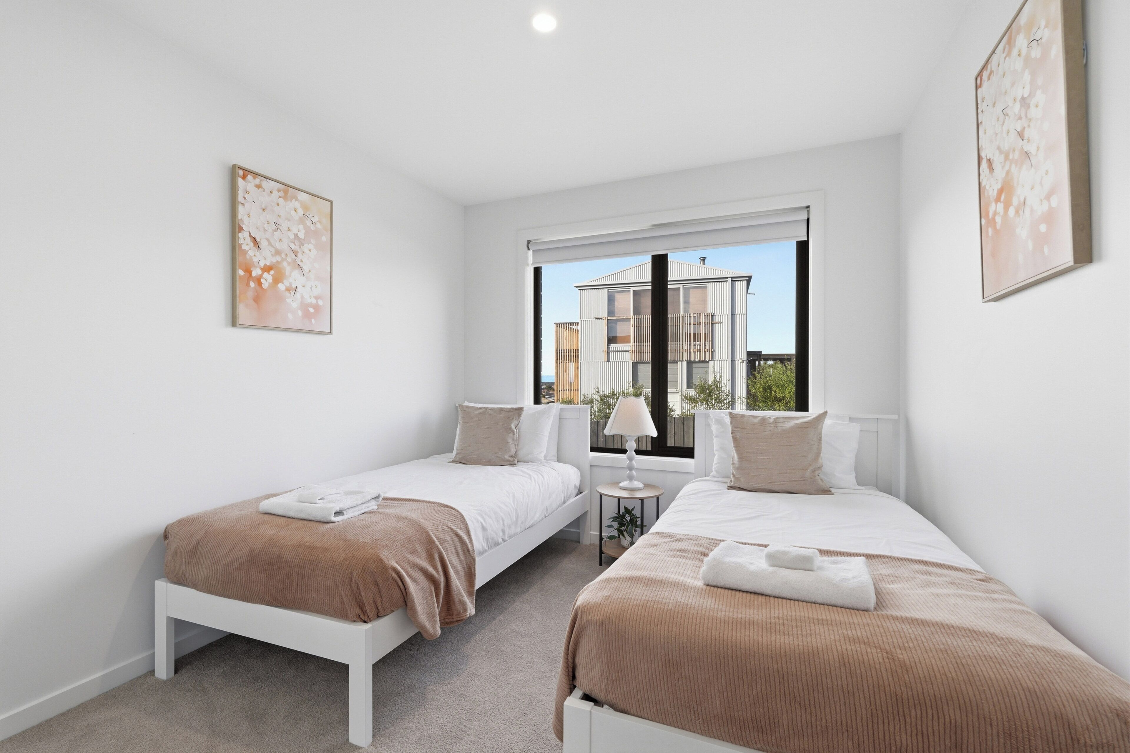 Une chambre avec deux lits simples, une fenêtre donnant sur des immeubles et deux œuvres d’art encadrées accrochées aux murs.