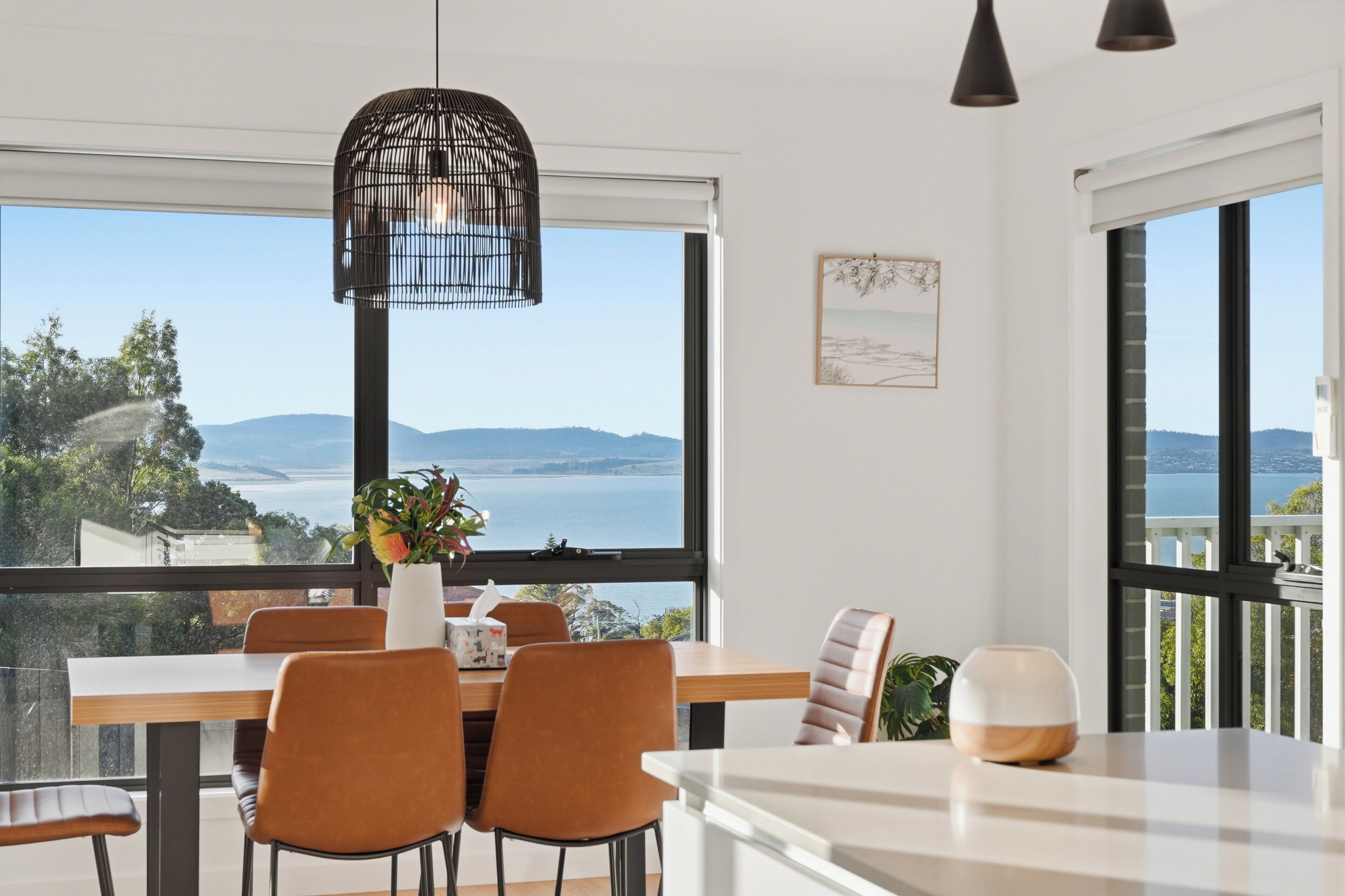A dining area with a view of the sea, a hanging light fixture, and a painting on the wall.