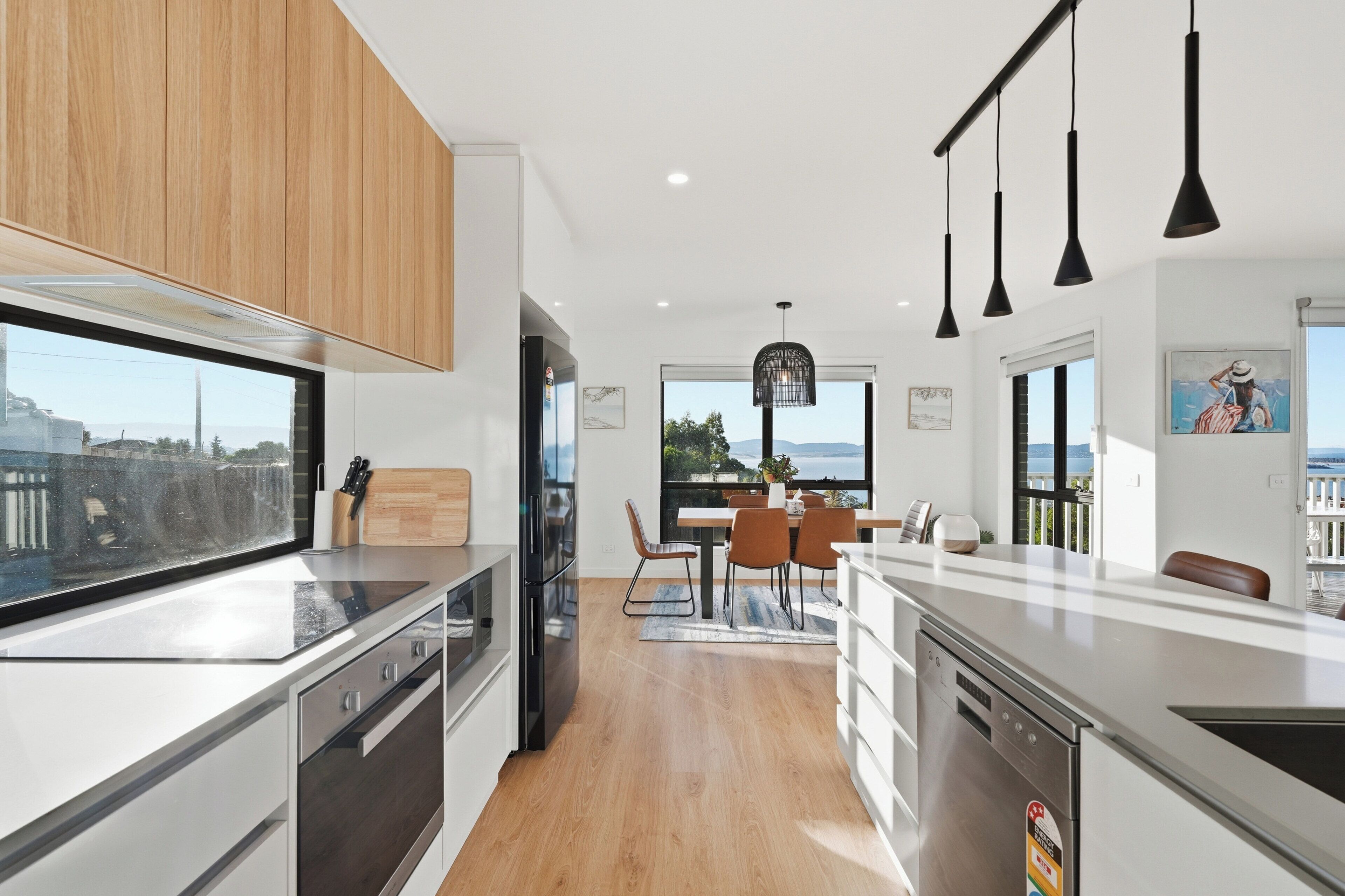 A modern kitchen with a view of the city, wooden cabinets, stainless steel appliances, and a dining area with a view.