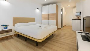 Una habitación de hotel moderna con cama, mesita de noche, televisor y armario.