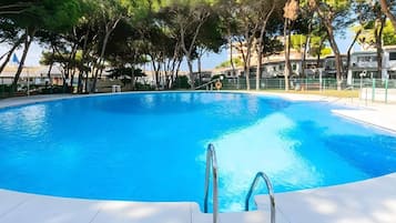 Une piscine d’un bleu éclatant, avec un escalier en métal menant à l’eau, entourée d’arbres et de bâtiments en arrière-plan.