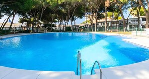 A clear blue swimming pool with a metal ladder leading into the water, surrounded by trees and buildings in the background. - Apartment 'Calypso' with Shared Pool, Wi-Fi and Air Conditioning (Mijas)