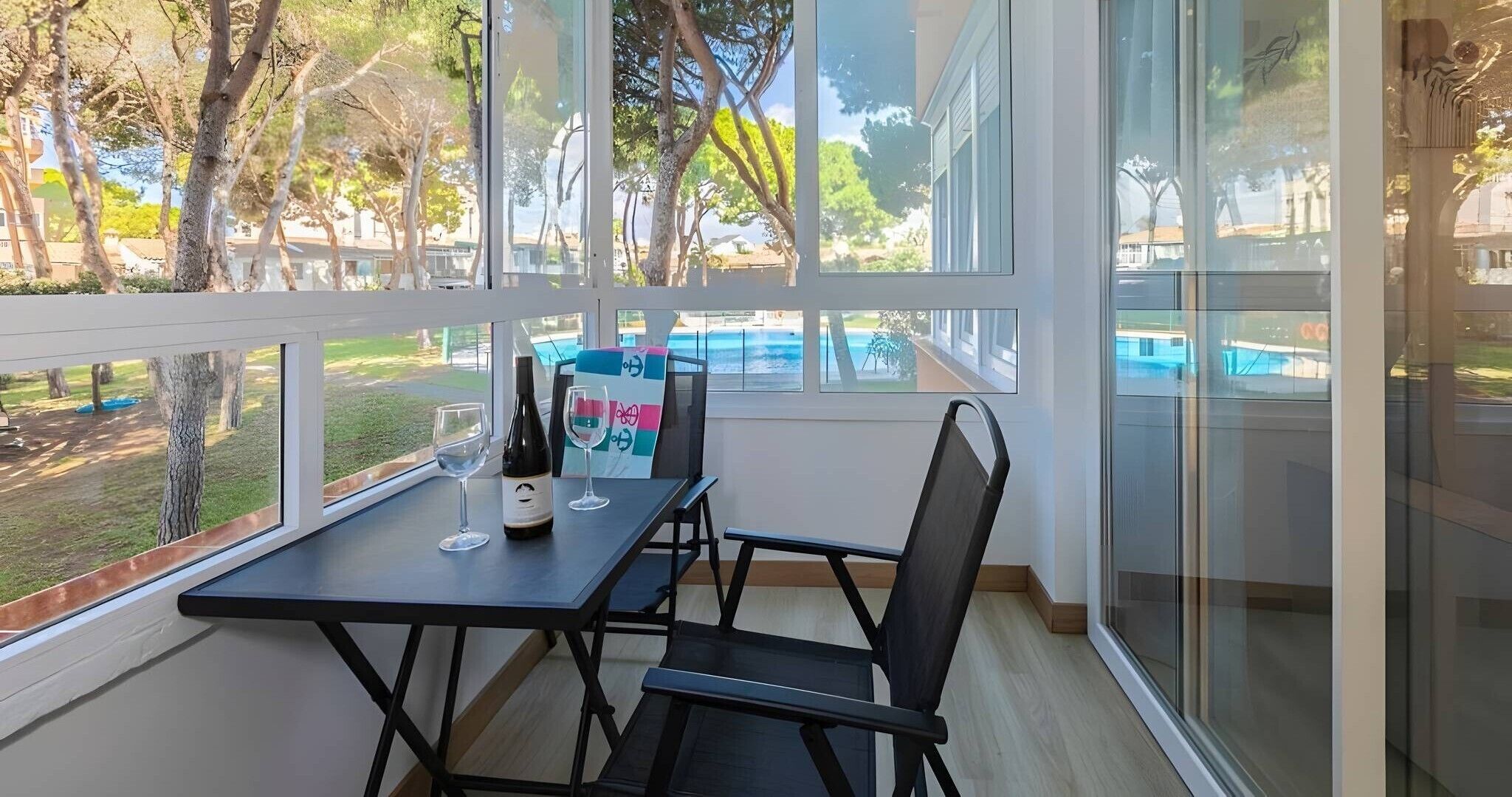 Un balcon avec une table et des chaises, une bouteille de vin et deux verres.