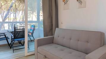 Una habitación con sofá, una mesa de comedor con sillas y vistas a árboles a través de un ventanal.