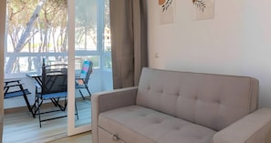 A room with a sofa, a dining table with chairs, and a view of trees through a glass door.