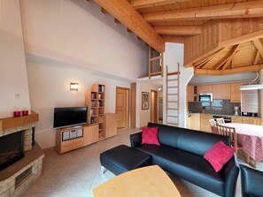 Ein geräumiger Wohnbereich mit einem schwarzen Sofa, einem Fernseher und einem Kamin.