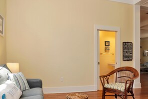 Ein Wohnzimmer mit einer Couch, einem Korbstuhl, einer Lampe und einer Tür zu einem anderen Raum.