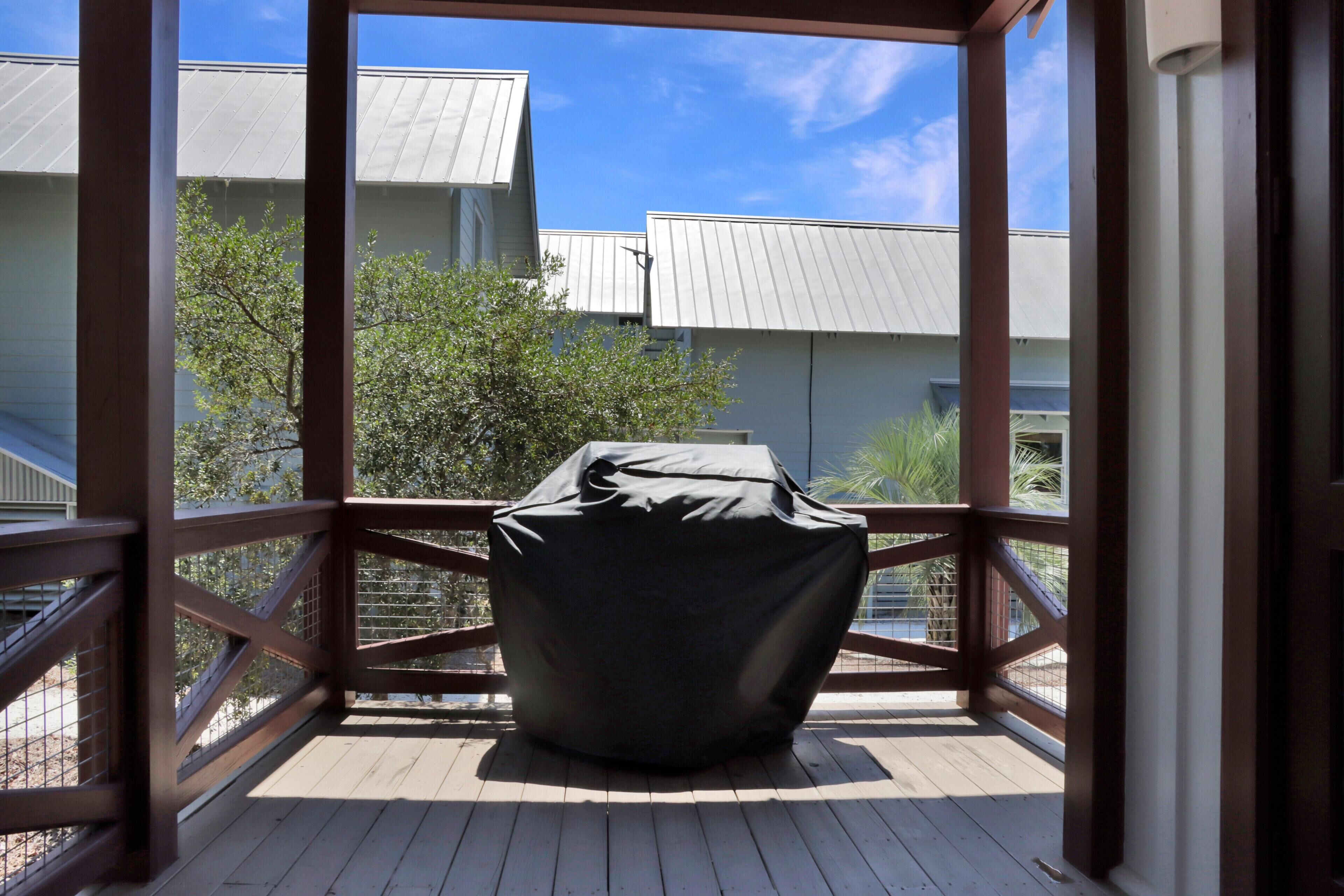 Un espace extérieur abrité, doté d’une terrasse en bois, d’un fauteuil en forme de sac de haricots noir et offrant une vue sur des bâtiments aux toits métalliques.
