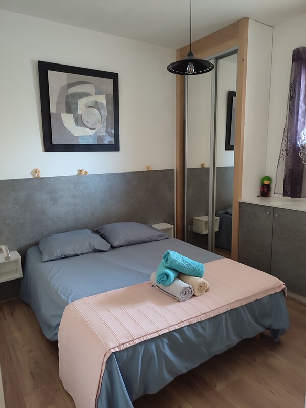 A bedroom with a bed, a bedside table, a nightstand, a mirror, and a framed picture on the wall. - Calvi Center, beach 200 m away, 1-bedroom apartment: sleeps up to 4, air conditioning, balcony, free private parking. (Calvi)