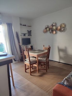 Ein Essbereich mit einem Holztisch und Stühlen, einem Fernseher auf einem Regal sowie dekorativen Wandbildern.