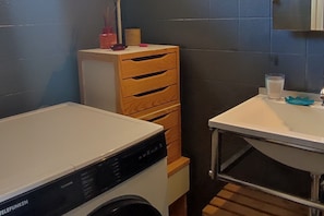 A compact laundry room with a washing machine, a wooden cabinet with drawers, and a sink with a glass of water. - Calvi Center, beach 200 m away, 1-bedroom apartment: sleeps up to 4, air conditioning, balcony, free private parking. (Calvi)