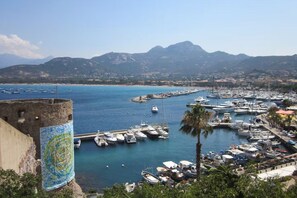 A coastal marina with boats docked, a historic tower, and mountains in the background. - Calvi Center, beach 200 m away, 1-bedroom apartment: sleeps up to 4, air conditioning, balcony, free private parking. (Calvi)