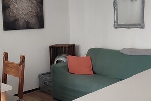 Ein Wohnzimmer mit einem grünen Sofa, einem Holzstuhl, einem kleinen Tisch, einer Heizung und einem gerahmten Bild an der Wand.