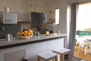 A modern kitchen with a fruit bowl, a microwave, and a dining area with a table and chairs. - Calvi Center, beach 200 m away, 1-bedroom apartment: sleeps up to 4, air conditioning, balcony, free private parking. (Calvi)