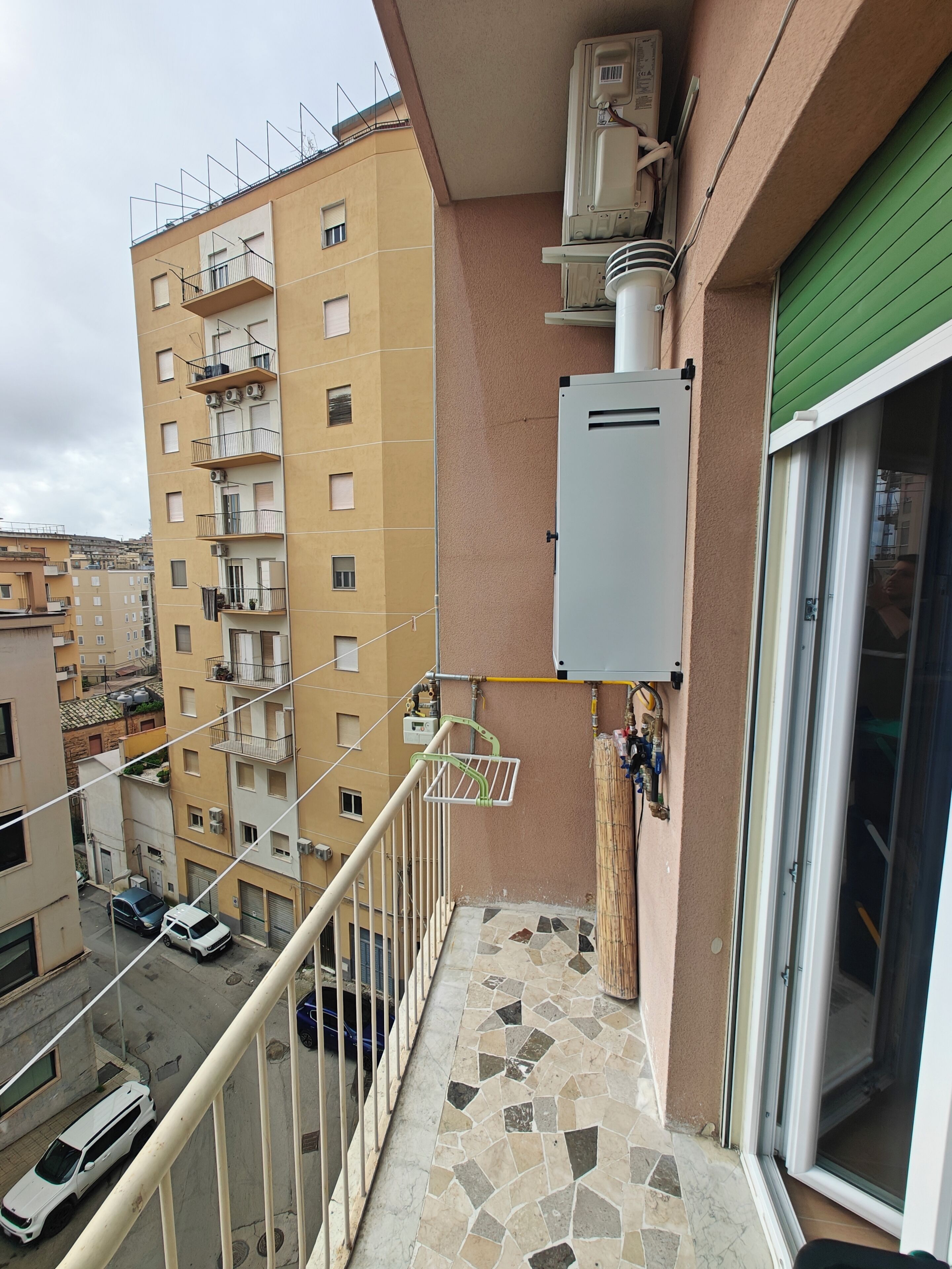 Uma varanda com piso de azulejos, guarda-corpo de metal e vista para edifícios próximos.