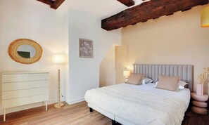 Un dormitorio con cama, lámparas de noche, cómoda, espejo y un cuadro en la pared.