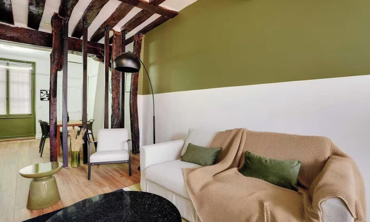 A living room with a white sofa, green cushions, a hanging floor lamp, and a dining area with chairs and a table.