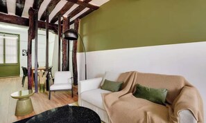 Ein Wohnzimmer mit einem weißen Sofa, grünen Kissen, einer stehenden Stehlampe und einem Essbereich mit Stühlen und einem Tisch.