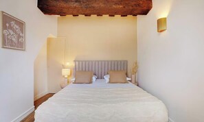 A bedroom with a large bed, a headboard, bedside lamps, and a wooden ceiling beam. - AN IDEAL BASE FOR EXPERIENCING THE VERY BEST OF THE FRENCH CAPITAL-SAINT GERMAIN (Paris)